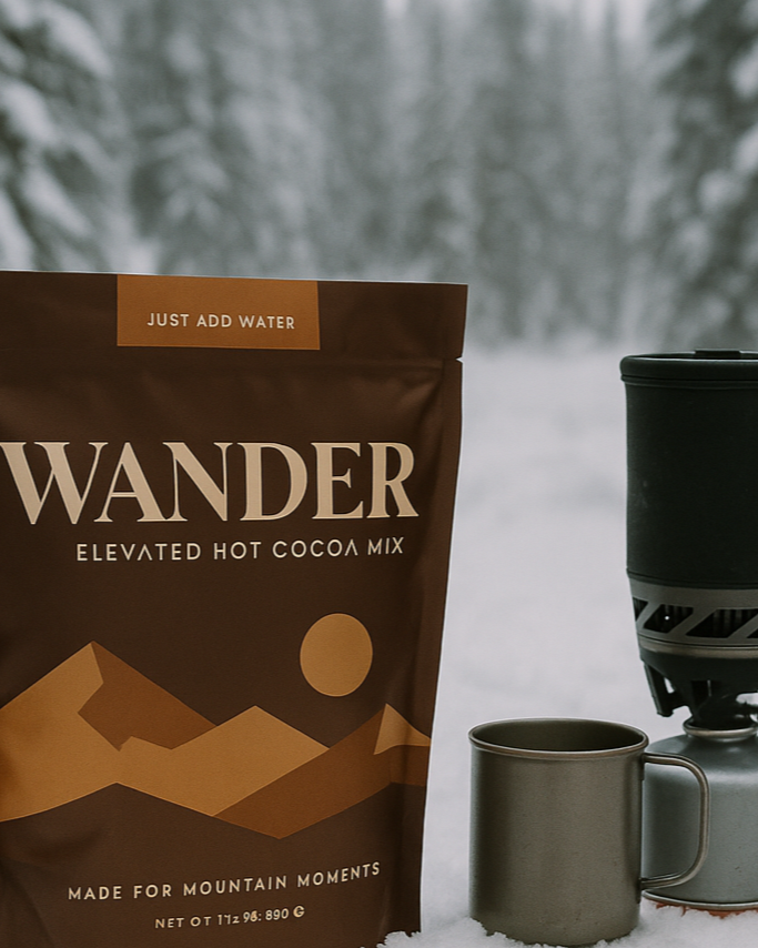 Wander hot cocoa mix package with a camping mug and stove in a snowy forest setting